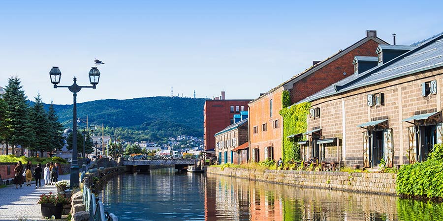 The Otaru Canal is lined with old fashioned brick buildings and warehouses on a bright day.
