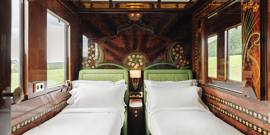 A beautifully decorated cabin on the Venice Simplon-Orient-Express: the room contains Art Deco details such as wood panelled walls with decorative flowers designs, patterned green furniture and golden details.